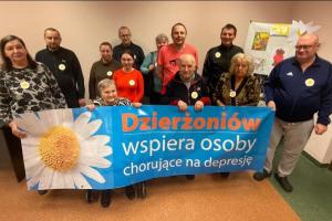Grupa osób trzyma baner z napisem Dzierzoniów wspiera osoby chorujące na depresję.