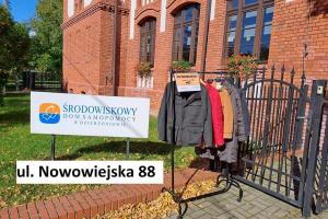 W tle widać duży, czerwony budynek Środowiskowego Domu Samopomocy, na pierwszym planie wieszak i wiszące na nim  kurtki