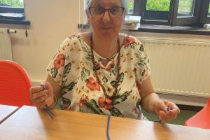 kobieta w okularach, w kwiecistej bluzce siedzi za stołem i pozuje do zdjęcia ze sznurkiem do makramy
