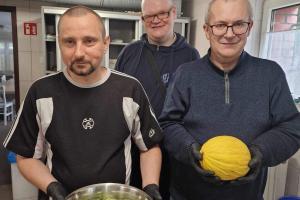 na zdjęciu widać trzech panów, pierwszy trzyma miskę z sałatką, drugi trzyma żółtego melona, trzecia osoba stoi po środku i uśmiecha się do fotografującegoa