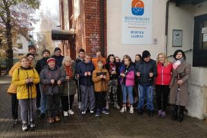 Przed budynkiem Środowiskowego Domu grupa osób pozuje do zdjęcia z kijkami do nordic walkingu. Wszyscy ubrani są w kurtki.