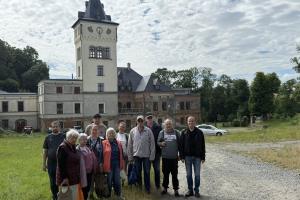 Na pierwszym planie stoi grupa osób, uczestników wycieczki. W tle znajduje się zamek