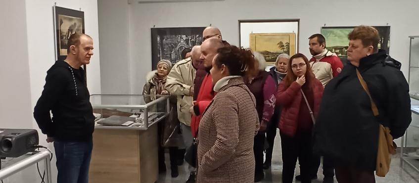 Pomieszczenie izby pamięci. Grupa osób slucha pana przewodnika