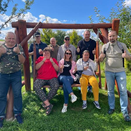 Wyświetl większy obrazek Dziewięć osób pozuje do zdjęcia, w tle widać drzewa i pogodne niebo. Wszyscy są uśmiechnięci i trzymają kciuki w górę