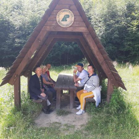 Wyświetl większy obrazek Pod drewnianą wiatą siedzą uczestnicy wycieczki 5 osób