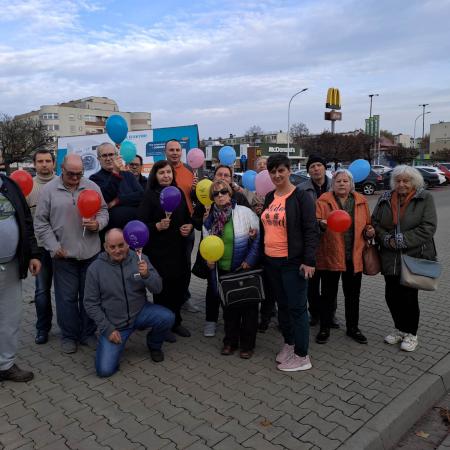 Wyświetl większy obrazek Uczestnicy wycieczki pozują do zdjęcia na chodniku. W rękach mają kolorowe balony. W tle widoczne logo znanej resteuracji 