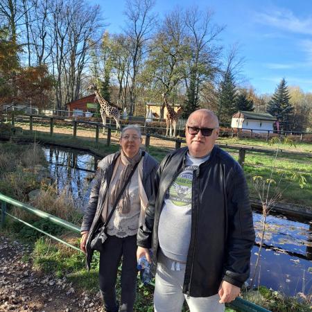 Wyświetl większy obrazek dwie osoby, kobieta i mężczyzna stoją na tle wybiegu dla żyraf.