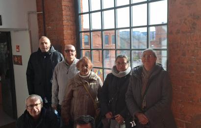 7 osób stoi na tle wielkiego okna oraz ceglanej ściany. Manufaktura Łódź