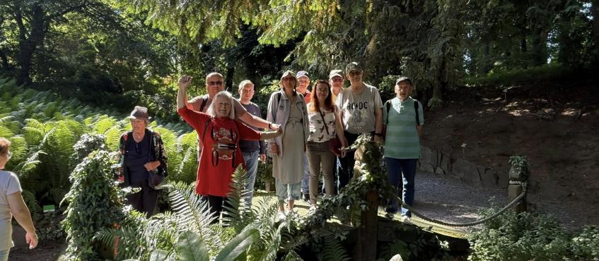 grupa osób pozuje na łonie natury. W tle widać paprocie oraz drzewa
